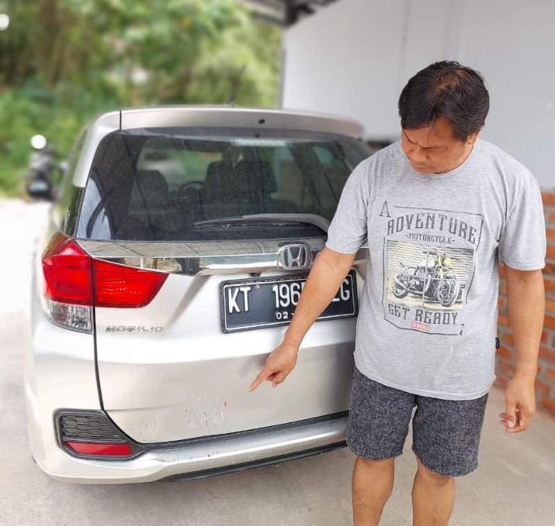 Pamuji menunjukkan bekas tabrakan di bagian belakang mobilnya.
