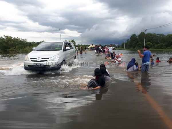 MAIN AIR: Belasan warga bermain air yang menggenangi kilometer 36 jalan Pangkalan Bun-Kotawaringin Lama, Kabupaten Kotawaringin Barat, Selasa (22/9).(GUSTI HAMDAN/RADAR SAMPIT)