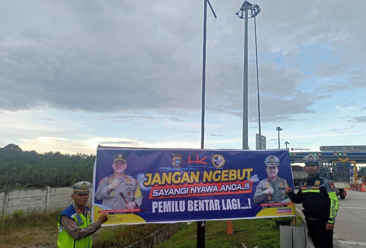 Petugas Sat PJR Ditlantas Polda Riau berfoto di spanduk yang dipasang di pintu TOL Pekanbaru-Dumai, Rabu (17/1/2024).