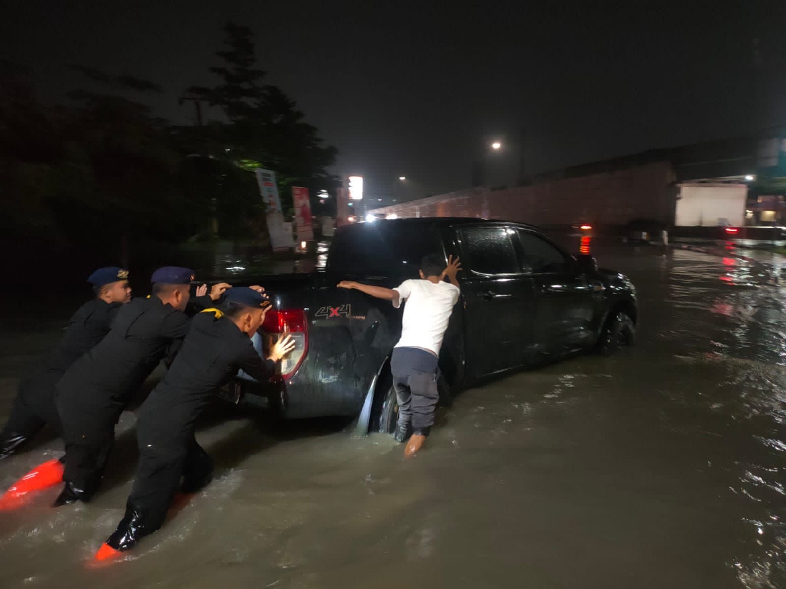 Petugas kepolisian membantu pengendara mendorong kendaraan mogok di tengah banjir di salah satu ruas jalan dalam Kota Pekanbaru, Selasa (23/1/2024) malam.