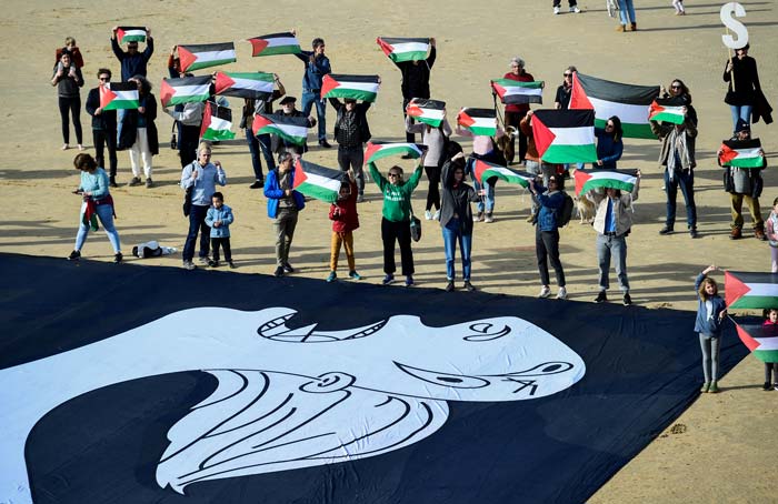 Para pengunjuk rasa memegang kanvas yang menggambarkan seorang ibu dan mengibarkan bendera Palestina di bawah slogan &ldquo;SOS Gaza&rdquo;, di pantai La Concha di Kota Basque, Spanyol, Ahad (28/1/2024).