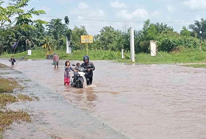 Dibantu anak-anak sekitar, seorang pengendara sepeda motor mendorong sepeda motornya yang mogok setelah melewati banjir di Jalan Sembilang, Kecamatan Rumbai, Rabu (31/1/2024).