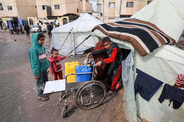 Seorang anak laki-laki mendorong kursi roda berisi jerigen plastik keluar dari tenda di kamp darurat bagi pengungsi Palestina di Rafah, Jalur Gaza Selatan, Senin (29/1/2024).