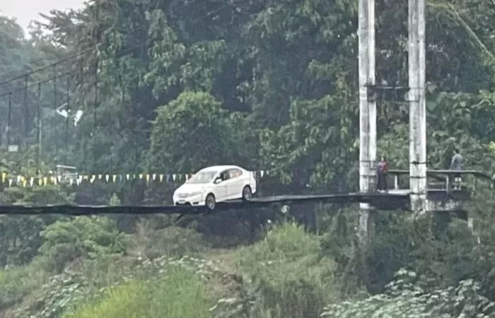 Seorang wanita dan mobil sedannya yang terjebak di jembatan gantung kecil di atas Sungai Yom, Thailand.
