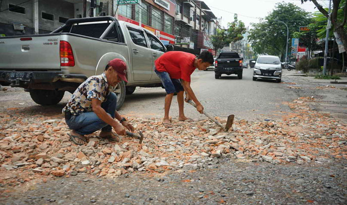 Warga secara swadaya menimbun lubang di Jalan M Yamin dengan material pecahan batu sisa, Jumat (23/2/2024).