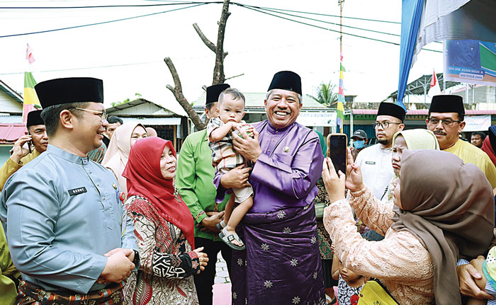Bupati Siak Alfedri menggendong seorang anak saat pemberian makanan tambahan dalam Program Bujang Kampung ke-100 bersama PT BSP di Kecamatan Tualang, Jumat (8/3/2024).