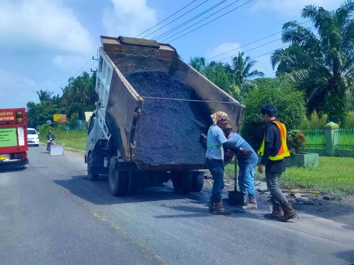 Pekerja melalukan perbaikan jalan raya Pasir Putih, Kampar, Riau, baru-baru ini.