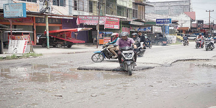 Pengendara melewati Jalan Darma Bakti, Kecamatan Payung Sekaki yang mengalami rusak parah, Rabu (24/4/2024).