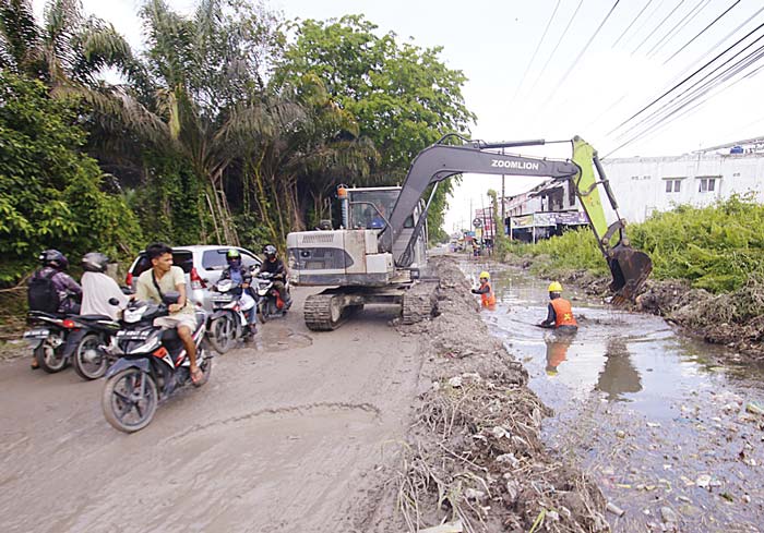 Para pekerja dari Dinas PUPR Kota Pekanbaru dibantu alat berat melakukan pengerjaan pembuatan saluran air (drainase) di Jalan Bangau Sakti.
