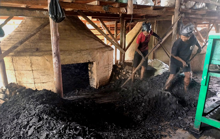 Dua pekerja wanita mengeluarkan arang batok kelapa yang baru selesai didinginkan untuk diayak kembali sebelum disimpan ke dalam gudang di Bengkalis, belum lama ini.
