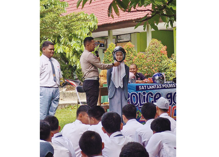 Personel Satlantas Polres Pelalawan memasangkan helm kepada siswi saat sosialisasi police goes to school di SMAN 1 Bandar Seikijang, Senin (13/5/2024).