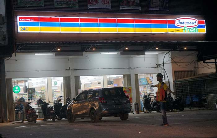 Petugas juru parkir mengatur kendaraan yang parkir di salah satu toko ritel modern di Jalan HR Soebrantas Panam, Ahad (9/6/2024) malam.