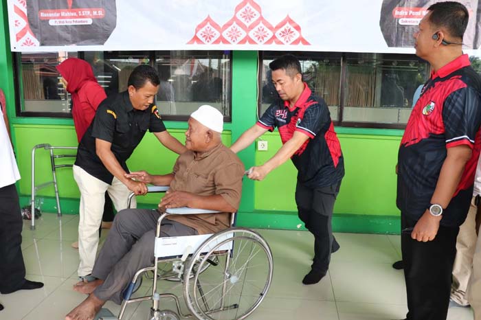 Pj Wako Pekanbaru Risnandar Mahiwa mendorong kursi roda yang diberikan kepada salah seorang penyandang disabilitas di Masjid Al-Kautsar.