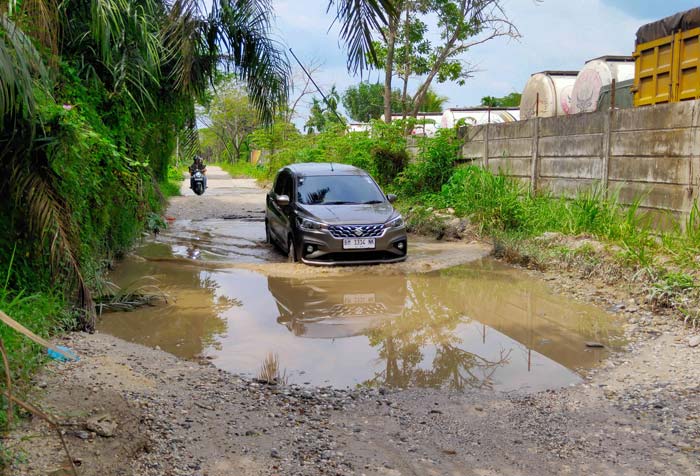 Pengen&shy;dara melintas di Jalan Payung Sekaki yang berlubang dan tergenang air, per&shy;sisnya di dekat Kantor Camat dan Polsek Payung Sekaki, Selasa (18/6/2024).