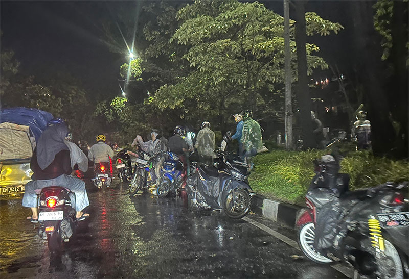 Sejumlah pengendara sepeda motor tampak mengangkat kendaraan untuk berpindah ke jalur yang aman dari banjir di Jalan Arifin Achmad, Kota Pekanbaru, Jumat (21/6/2024) malam.