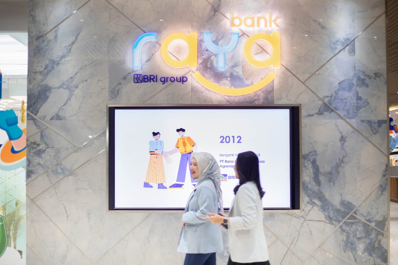 Dua pegawia melintas di depan logo Bank Raya, bank digital BRI Group, baru-baru ini.
