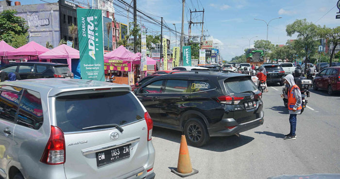 PARKIR: Juru parkir mengatur kendaraan di bahu Jalan Soebrantas, Panam, Pekanbaru, Ahad (7/7/2024). Sejumlah pengunjung mengaku kesal karena diminta retribusi parkir Rp5.000 untuk mobil dan Rp3.000