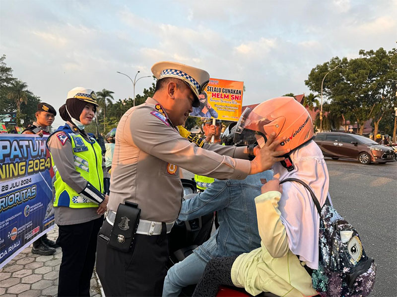 Dirlantas Polda Riau Kombes Pol Taufiq Lukman saat memasangkan helm kepada siswi yang melintas di Jalan Diponegoro, Pekanbaru, Jumat (19/7/2024) pagi.