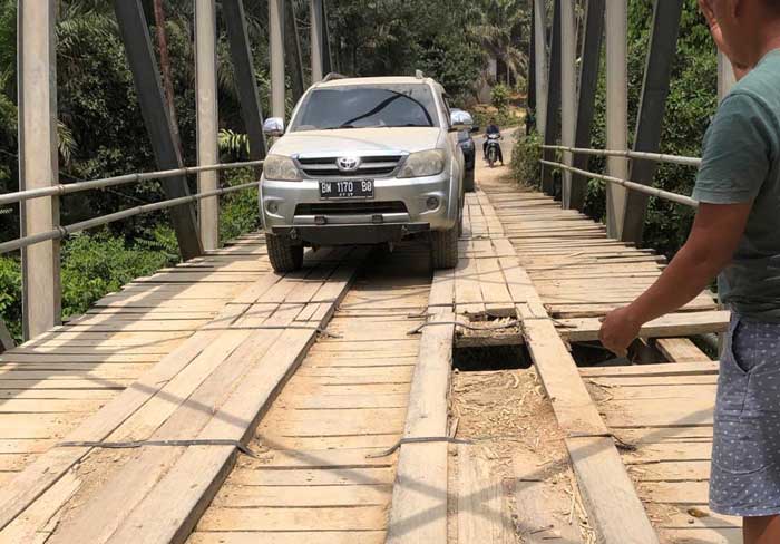 Salah seorang warga memandu mobil saat melintas di jembatan rusak di Kecamatan Batang Cenaku, baru-baru ini.