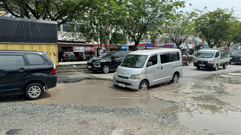 BERLUBANG: Kendaraan melewati lubang besar berisi genangan air di badan Jalan Soekarno Hatta, simpang Jalan Kaharuddin Nasution, Rabu (7/8/2024).