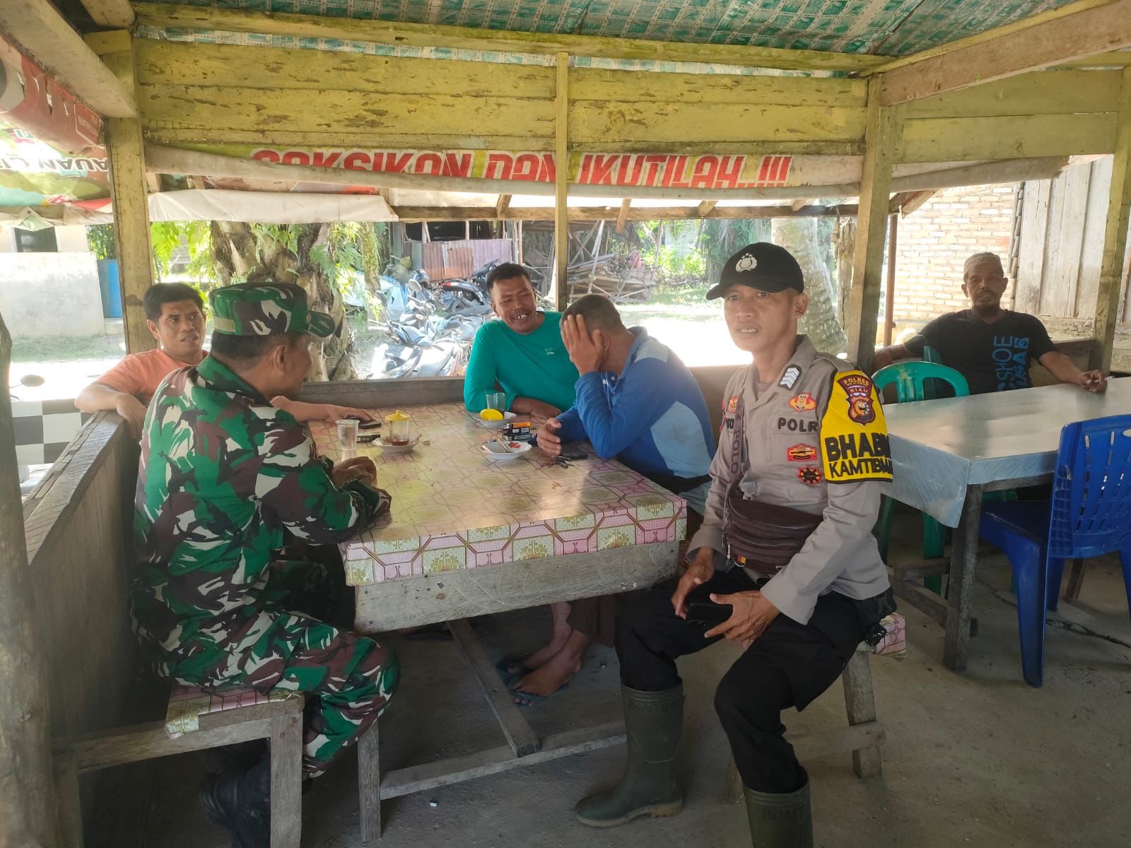 Petugas TNI-Polri di Kecamatan Langgam, Kabupaten Pelalawan saat duduk bersama warga di kedai kopi untu mengajak warga menjaga Kamtibmas selama Pilkada, Senin (23/9/2024).