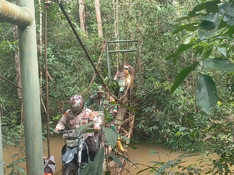Bripka Pane dari Polsek Ukui bersama Praka Faizul dari TNI menyusuri jalan setapak yang dikelilingi hutan lebat dan jembatan ekstrem ke pelosok desa demi Pilkada aman dan damai.