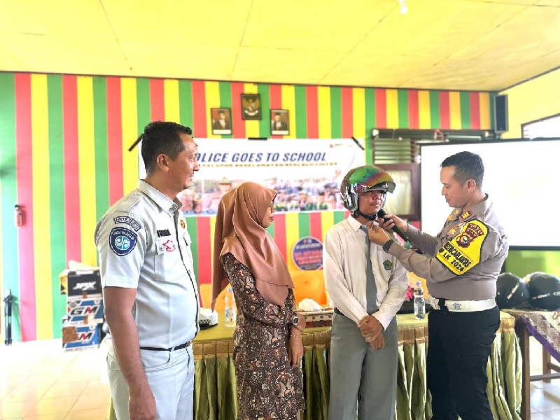 Kasat Lantas AKP Kaliman Siregar SH MM memakaikan helm kepada perwakilan siswa saat sosialisasi tekan angka fatalitas kecelakaan serta cooling system di MAN 1 Siak, Selasa (5/11/2024).  ////