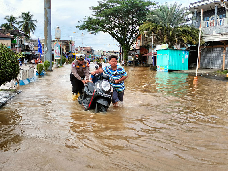 Personel Satlantas Polres Rohul membantu mendorong motor pengendara kendaraan roda dua saat menerobos banjir yang merendam ruas Jalan Tuanku Tambusai Pasirpengaraian, Sabtu (23/11/2024).