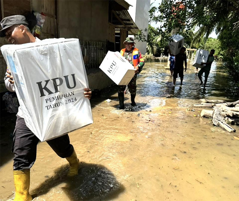 Personel Polsek Kepenuhan, TNI, PPK mengangkat Logistik Pilkada 2024 menuju PPS Desa Rantau Binuang Sakti yang sejumlah dusun terendam banjir dari luapan air sungai setempat, Selasa (26/11/2024).