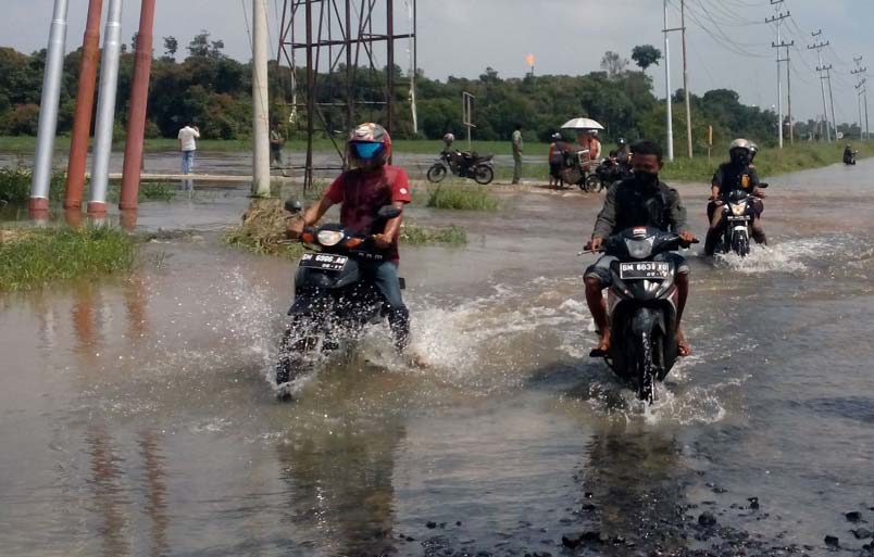 Pengendara sepeda motor berusaha menerobos akses jalan poros Desa Lubuk Ogung menuju Kelurahan Langgam, Kecamatan Langgam, Kabupaten Pelalawan yang digenangi air, Ahad (1/12/2024).