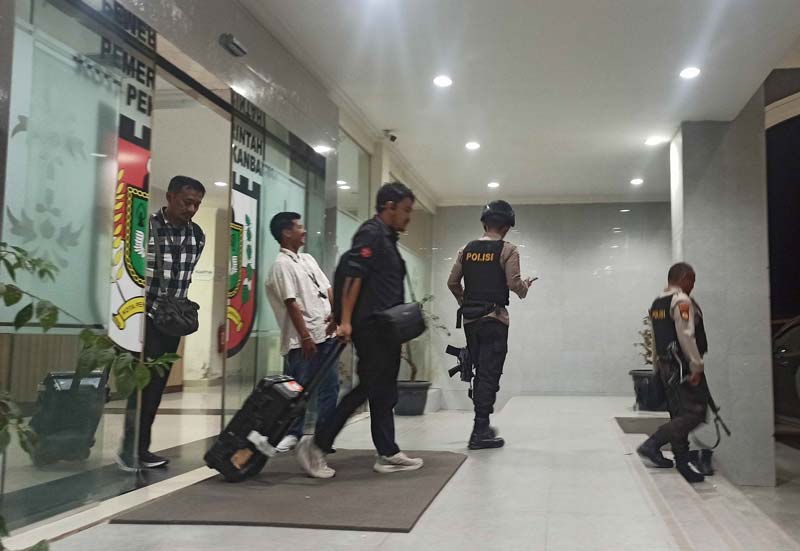 Penyidik KPK dikawal petugas kepolisian membawa koper usai menggeledah kantor Dinas Perkim Pekanbaru di Gedung Limas Kompleks Perkantoran Tenayan Raya, Senin (9/12/2024).
