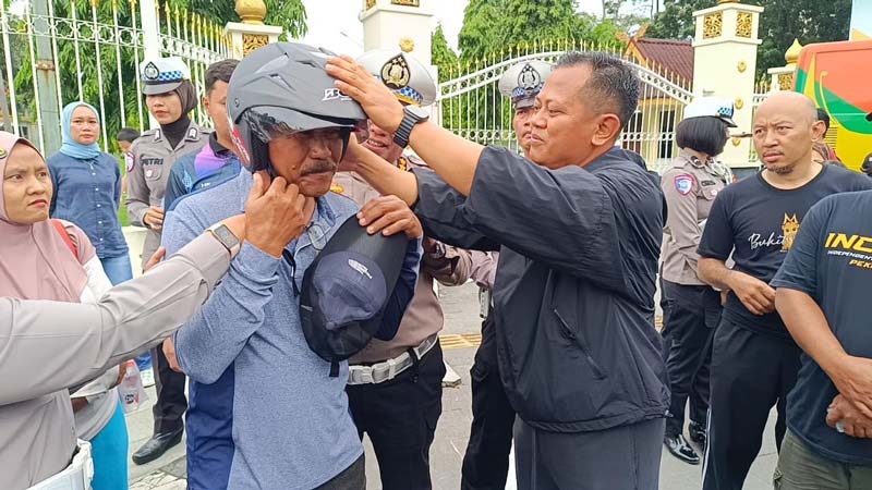 Dirlantas Polda Riau Kombes Pol Taufiq Lukman memasang helm SNI gratis kepada warga pengunjung CFD, Ahad (19/1/2025).