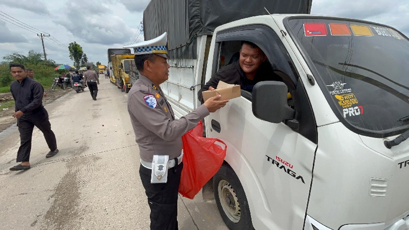 Personel Satlantas Polres Pelalawan menyerahkan bantuan nasi kotak gratis kepada pengguna jalan yang terjebak antrean kendaraan di Jalintim Km 74 yang terendam banjir, Ahad (26/1/2025) siang.