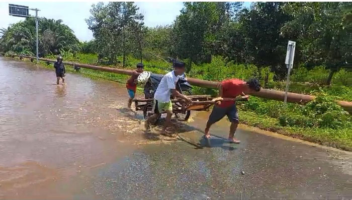 Membantu warga menyeberangkan sepeda motor menggunakan gerobak dengan bayaran Rp75 ribu di Jalan Lintas Tanjung Buton, Kampung Dosan, Kecamatan Pusako, Kabupaten Siak, Kamis (30/1/2025).