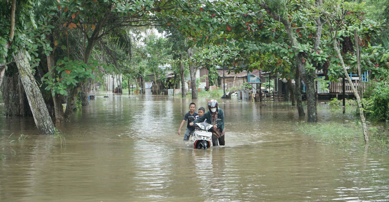 Seorang pria bersama dua orang anak mendorong sepeda motor yang mogok saat melewati banjir yang merendam Jalan Lembah Raya, Kamis (27/2/2025).