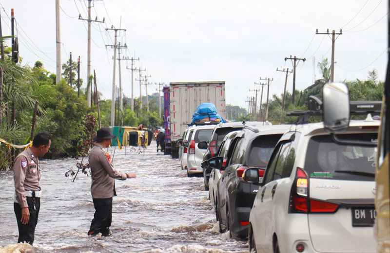 Personel Polres Pelalawan mengatur lalu lintas di Jalan Lintas Timur Km 83 Desa Kemang, Kecamatan Pangkalan Kuras, Kabupaten Pelalawan yang masih digenangi banjir.