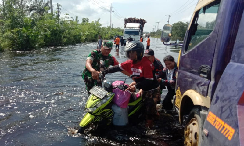 Petugas membantu pengendara sepeda motor yang menerobos banjir  di Jalan Lintas Timur Km 83 Desa Kemang, Kecamatan Pangkalan Kuras, Kabupaten Pelalawan.