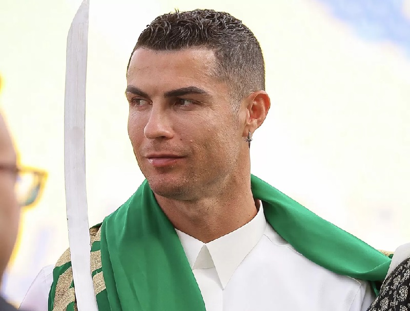 Cristiano Ronaldo dengan gamis putih dan sorban hijau memegang pedang.