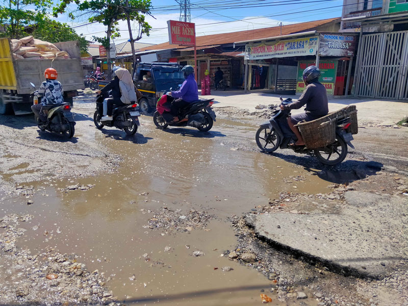 Pengendara melintas di Jalan Dharma Bakti yang mengalami kerusakan cukup parah dan tergenang, Ahad (20/4/2025).