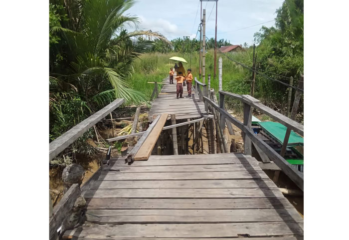 Pelajar Sekolah Dasar (SD) sedang melintasi jembatan dengan jembatan rusak parah di Kelurahan Seberang Tembilahan, Kecamatan Tembilahan, Inhil, Rabu (14/5/2025).