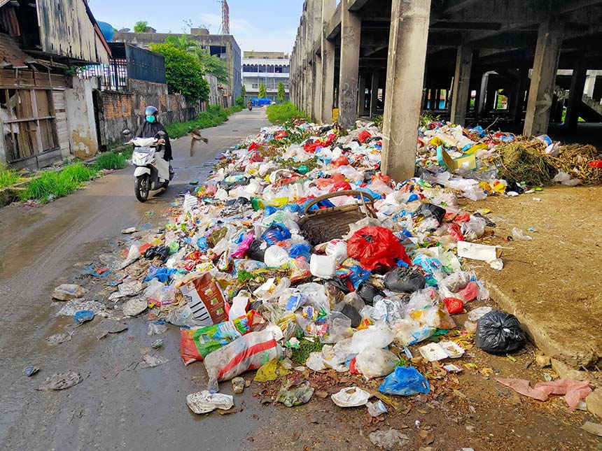 Pengendara motor melintas di dekat tumpukan sampah yang ada di bangunan Pasar Cik Puan yang belum selesai, Rabu (4/6/2025).