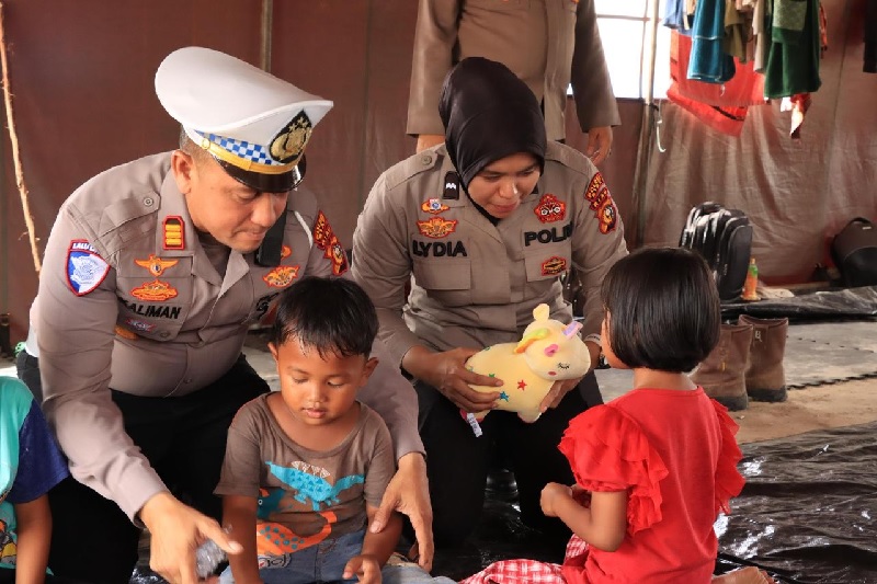 Kasatlantas Polres Siak AKP Kaliman Siregar SH MH memberikan mobil mobilan kepada dua anak karyawan PT SSL di tenda pengungsian di Kampung Tumang, Kecamatan Siak, Sabtu (14/6/2025).
