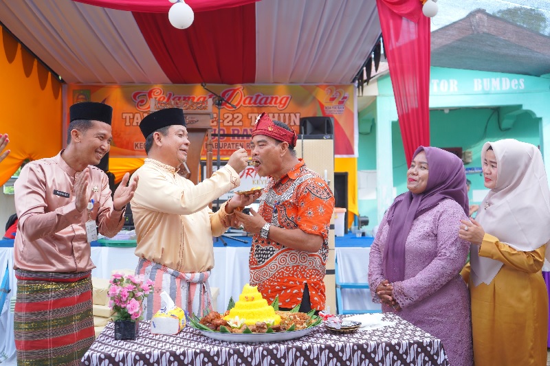 Wabup Rohul H Syafaruddin Poti SH MM menyuguhkan potongan nasi tumpeng kepada Kades Puo Raya Yasrizon dalam acara peringatan HUT ke 22 di kantor desa setempat, Jumat (20/6/2025).