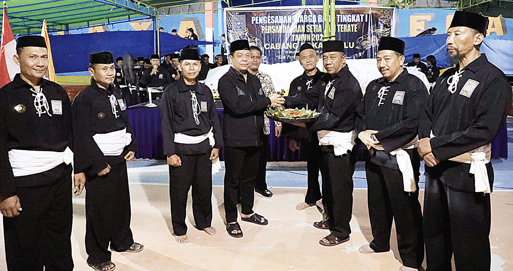 Wabup Rohul H Syafaruddin Poti SH MM didampingi Ketua PSHT Cabang Rohul Munandar SE MM (kiri) menerima bubur suro dari Koordinator Dewan Pengesah PSHT Pusat Madiun Wardoyo dalam acara pengesahan.