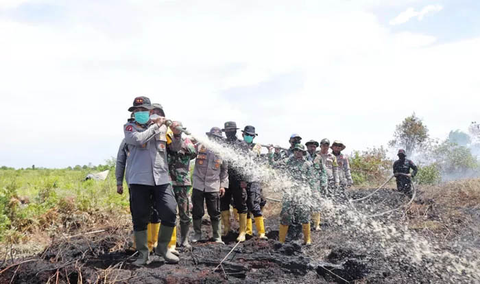Kapolda Riau Irjenpol Herry Heryawan dibantu personel melakukan penyiraman lahan terbakar di Kepenghuluan Sungai Segajah, Kubu, Sabtu (19/7/2025).