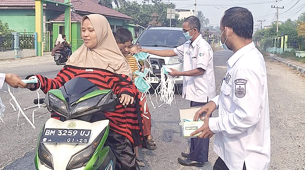 Pegawai Puskesmas Bangun Purba membagikan masker gratis kepada masyarakat di jalan raya saat kabut asap tipis menyelimuti Kabupaten Rohul, Rabu (23/7/2025)
