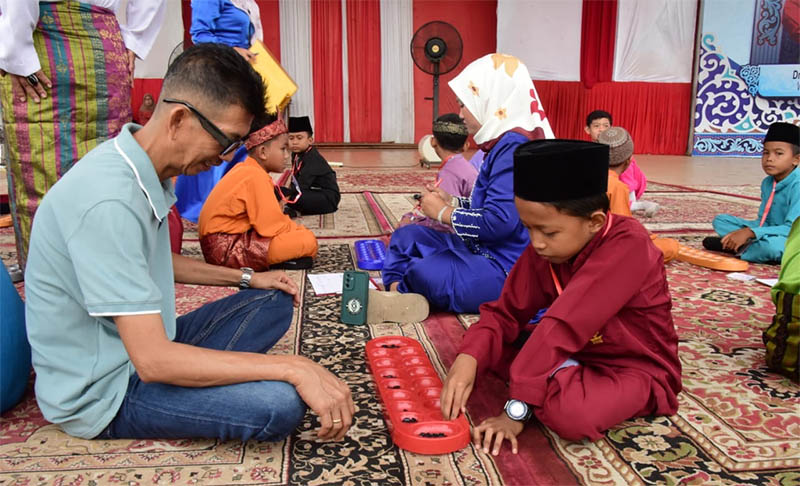 Staf Ahli Bupati Bengkalis Johansyah Syafri bermain congklak bersama anak SD di Lapangan Tugu Bengkalis, Sabtu (26/7/2025).