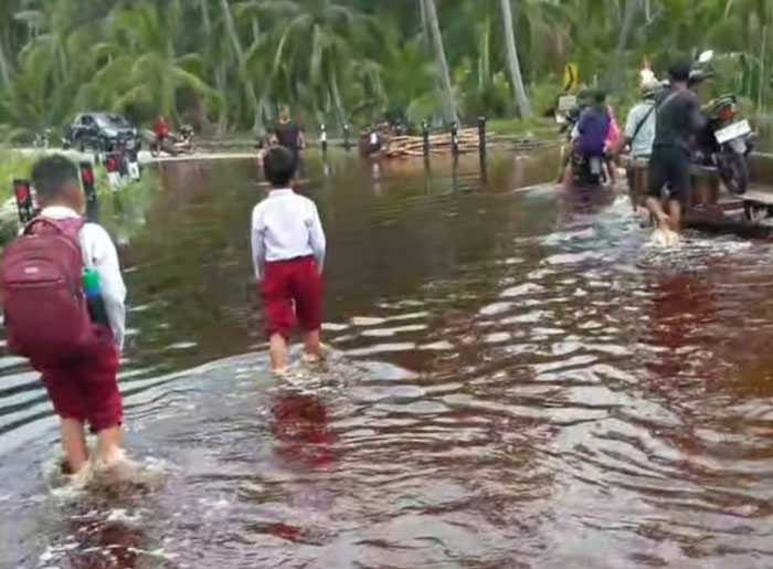 Murid sekolah dasar melintasi jalan yang terendam air pasang laut saat kembali dari sekolahnya di Desa Suka Maju Kecamatan Bantan, Bengkalis, Kamis (9/10/2025).