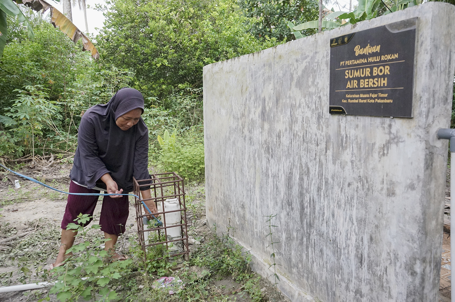 Seorang warga Sunarti memeriksa kondisi sumur bor air bersih dari Pertamina Hulu Rokan, Jumat (3/10/2025). Untuk memastikan fasilitas air bersih ini terus terjaga warga sepakat untuk membentuk pengurus pengelolaan air.
