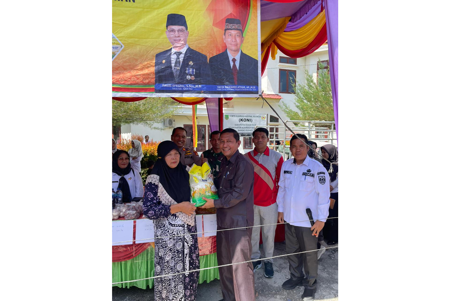 Kepala DKPP Rohil Cicik Mawardi Athar didampingi Camat Bangko Pusako Riwansyah (dua kanan)secara simbolis menyerahkan beras yang dijual pada kegiatan Gerakan Pangan Murah (GPM) di Kecamatan Bangko Pusako, Rabu (29/10/2025).